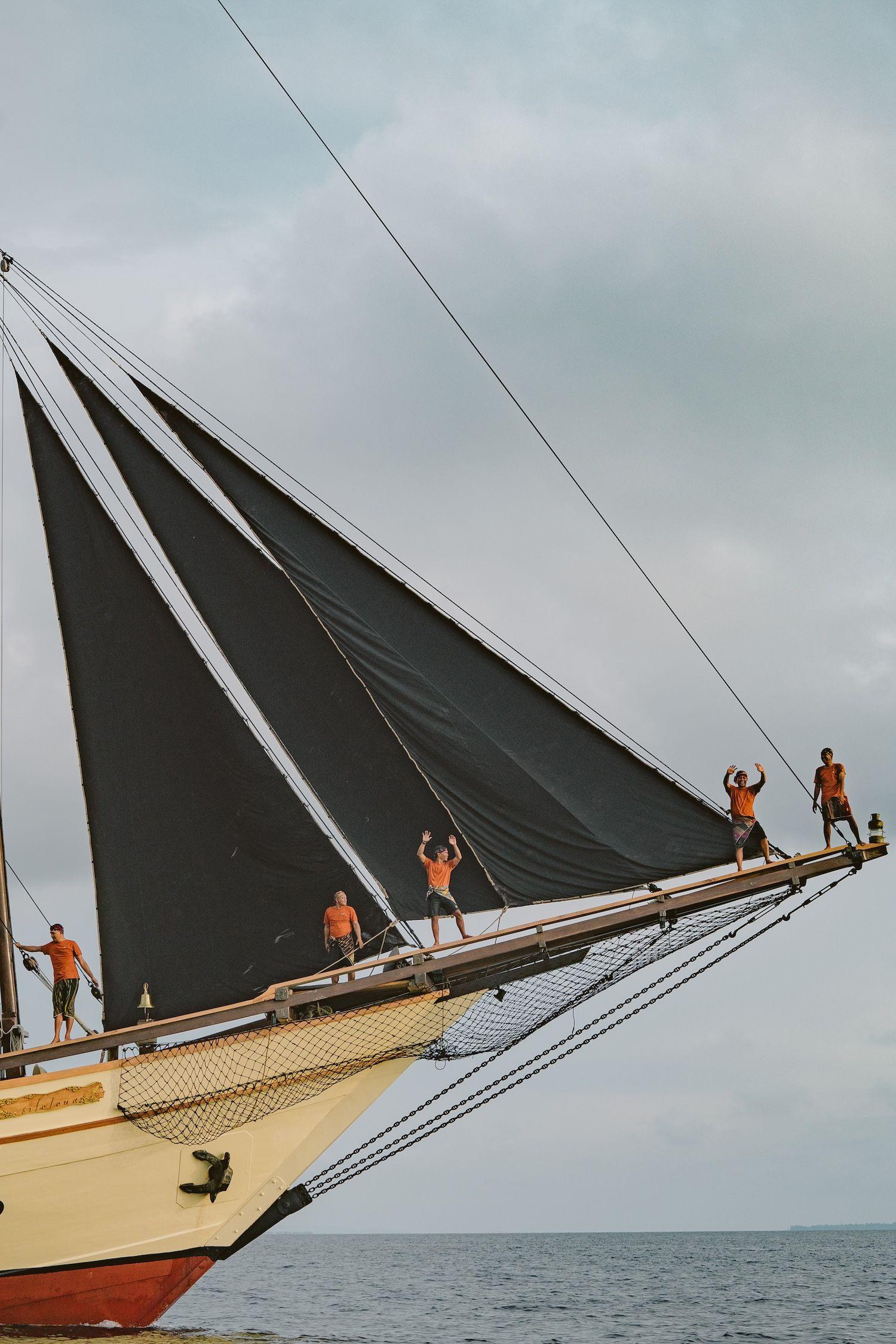 silolona boat, black sailing, few people stand near by the sail