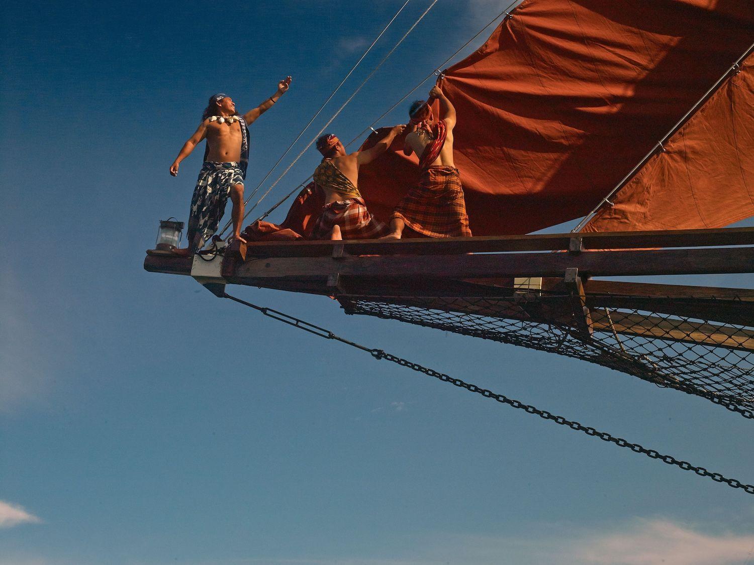 si datu bua boat, three people standing nearby sail, red sail, blue sky