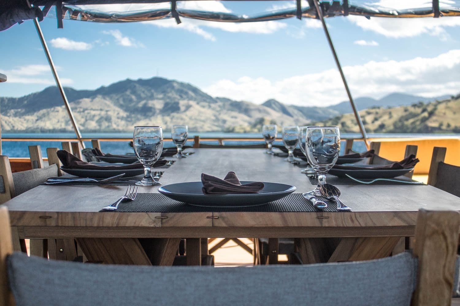 wooden dining table, glasses, black plate, green hills view, blue clear sky