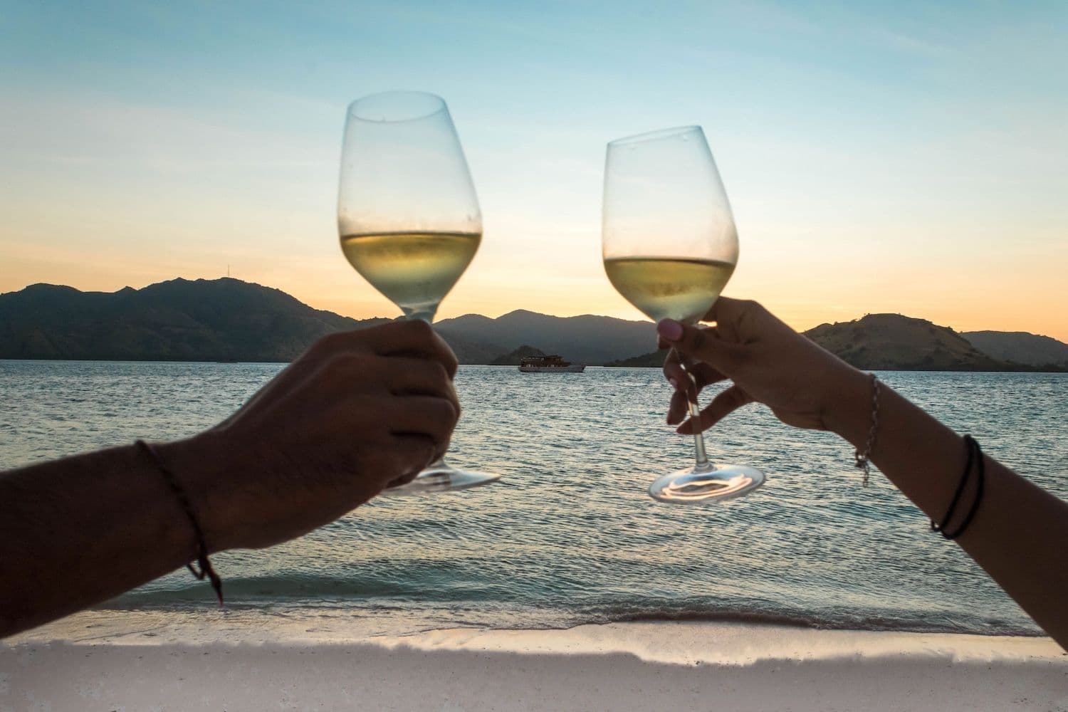 two people raise glass, blue sky, sea water, on the beach