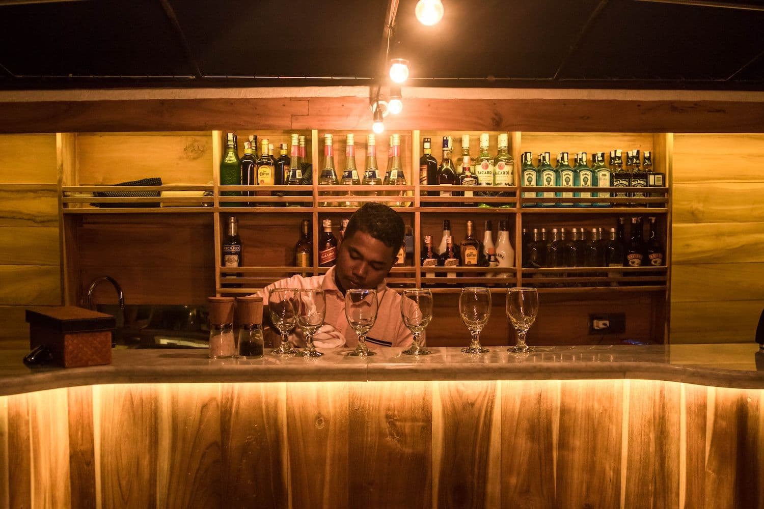 a man behind the bar table, yellow lights, bar table, drinks on the background