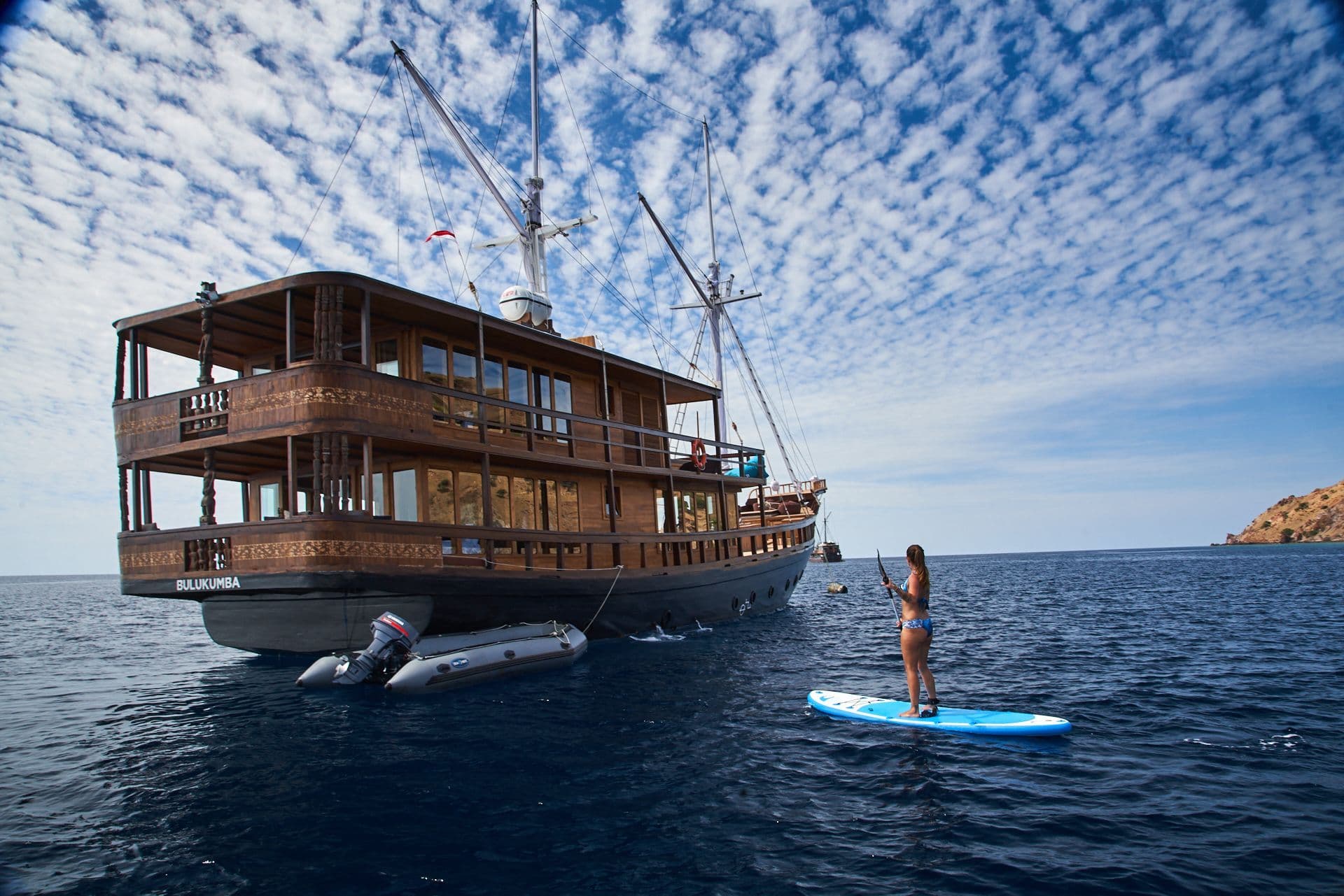 oracle boat landscape, open ocean, blue sky, cloudy sky, a woman standing on the paddleboard