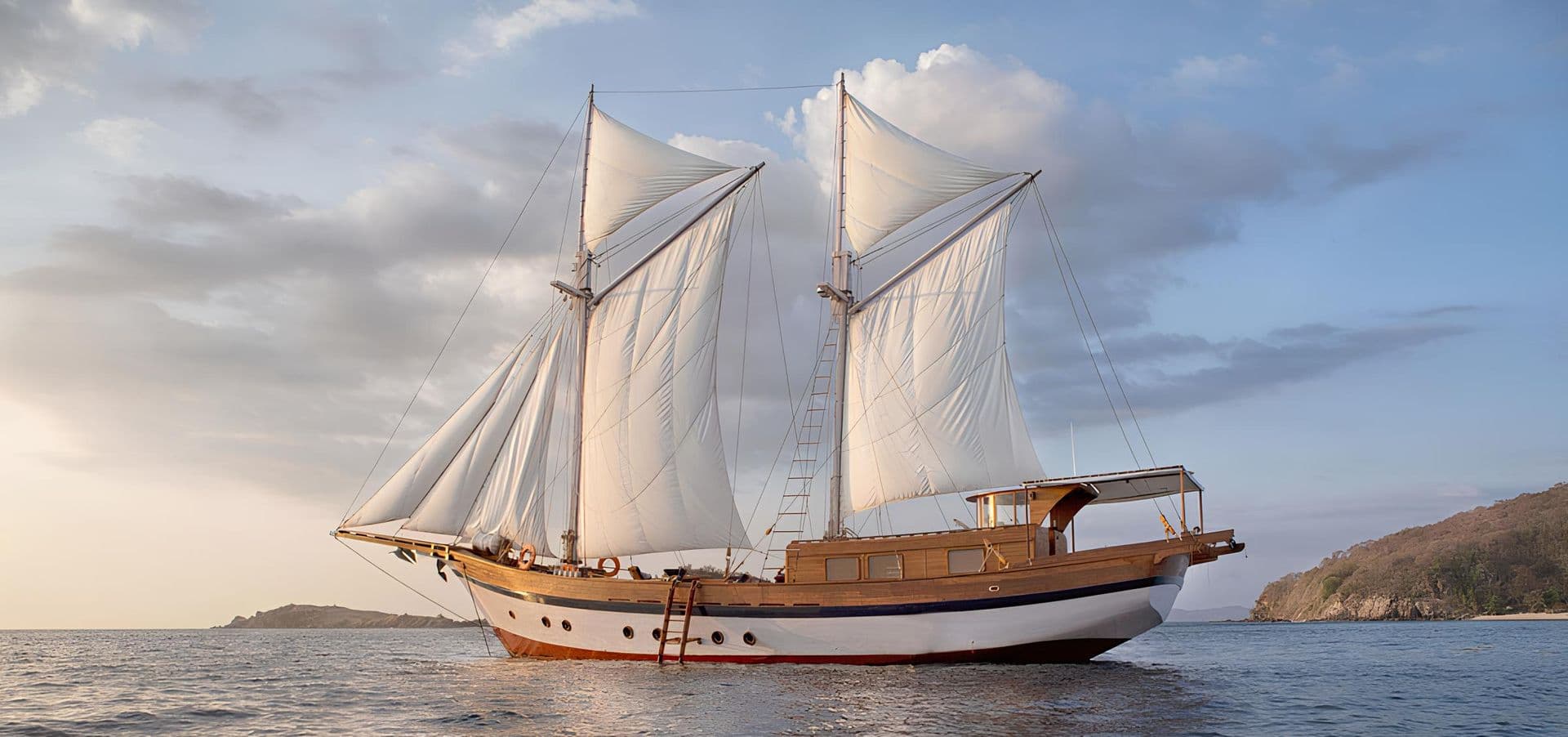 anne bonny boat, white sail, wooden exterior boat, beautiful view on the background